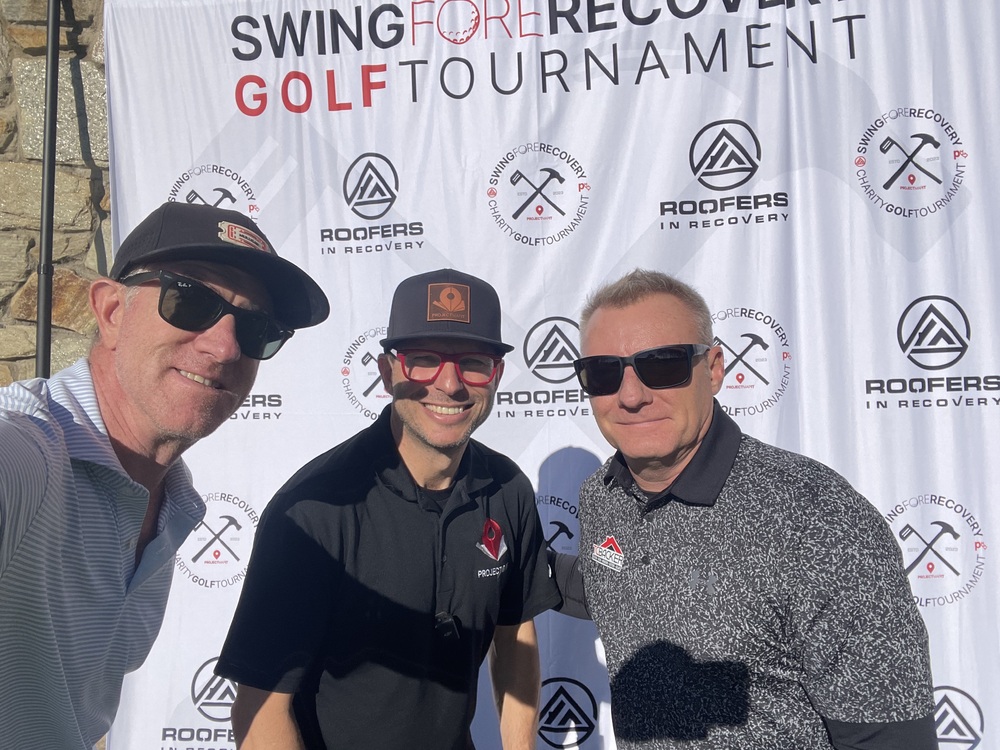 Three golfers pose in front of the Swing Fore Recovery Golf Tournament backdrop.