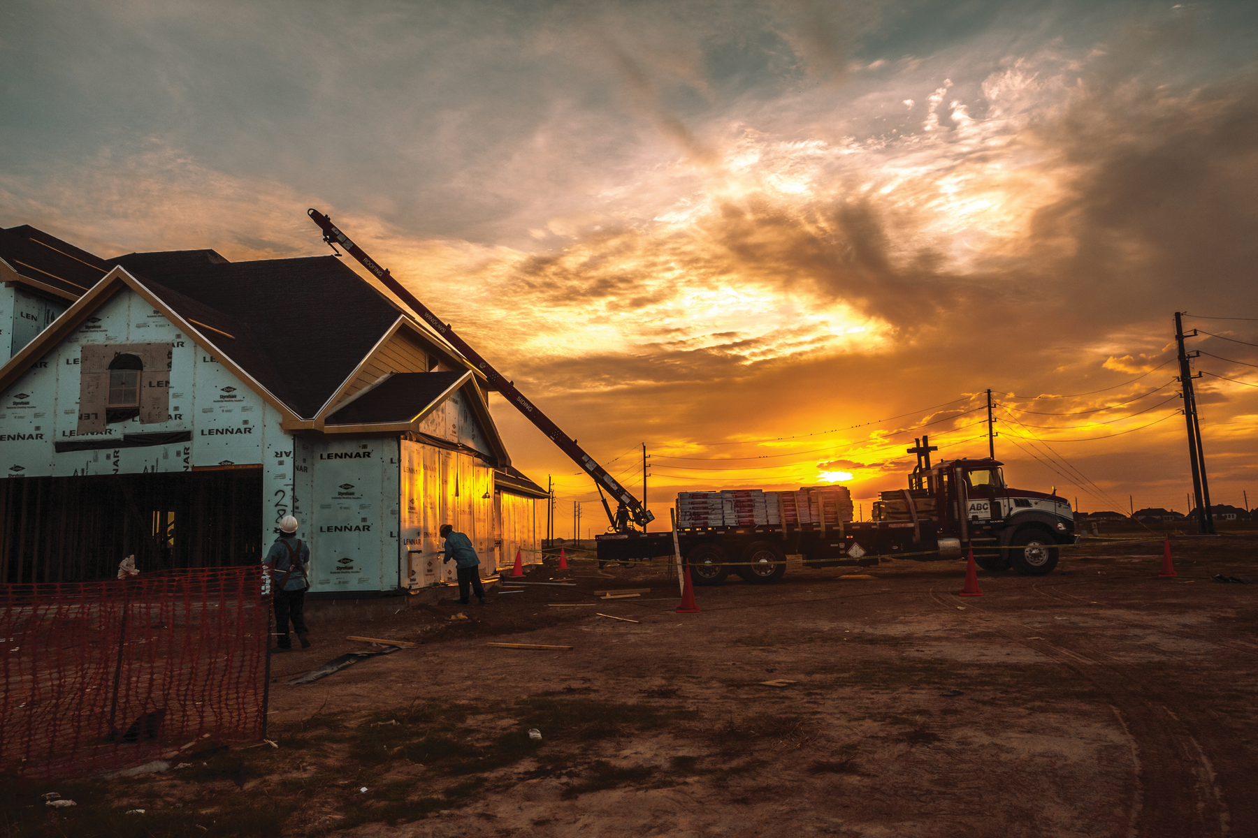 A truck carries ABC Supply materials to a construction site during sunset.